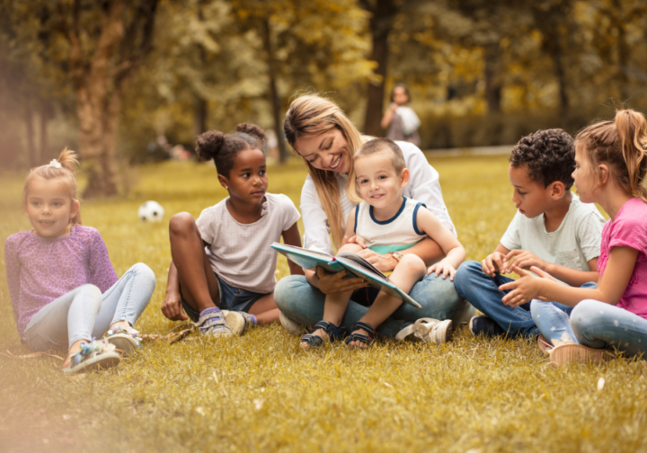 Children outdoors reading a book with a teacher
