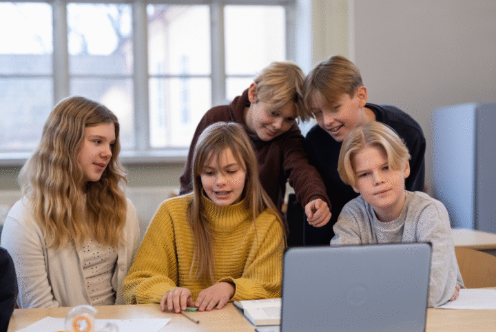 Elever i grundskolan samarbetar kring en bärbar dator under en lektion
