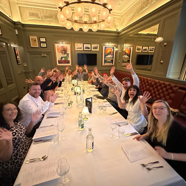 ILT Education UK team at adinner table with hands in the air