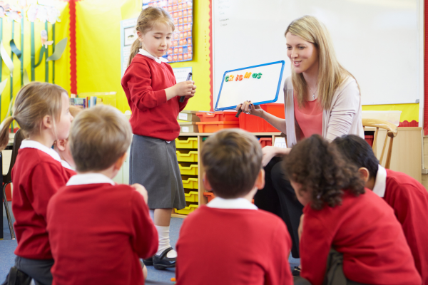 Teacher with 4 children in red school uniform teaching a lesson with a white board