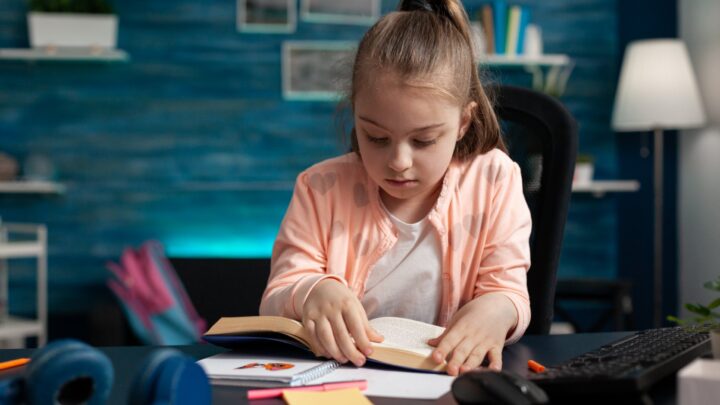 young girl in a pink top reading a book in a home office